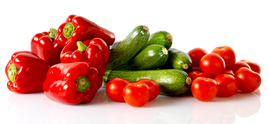 Fresh red bell peppers, zucchinis, and tomatoes arranged on white.