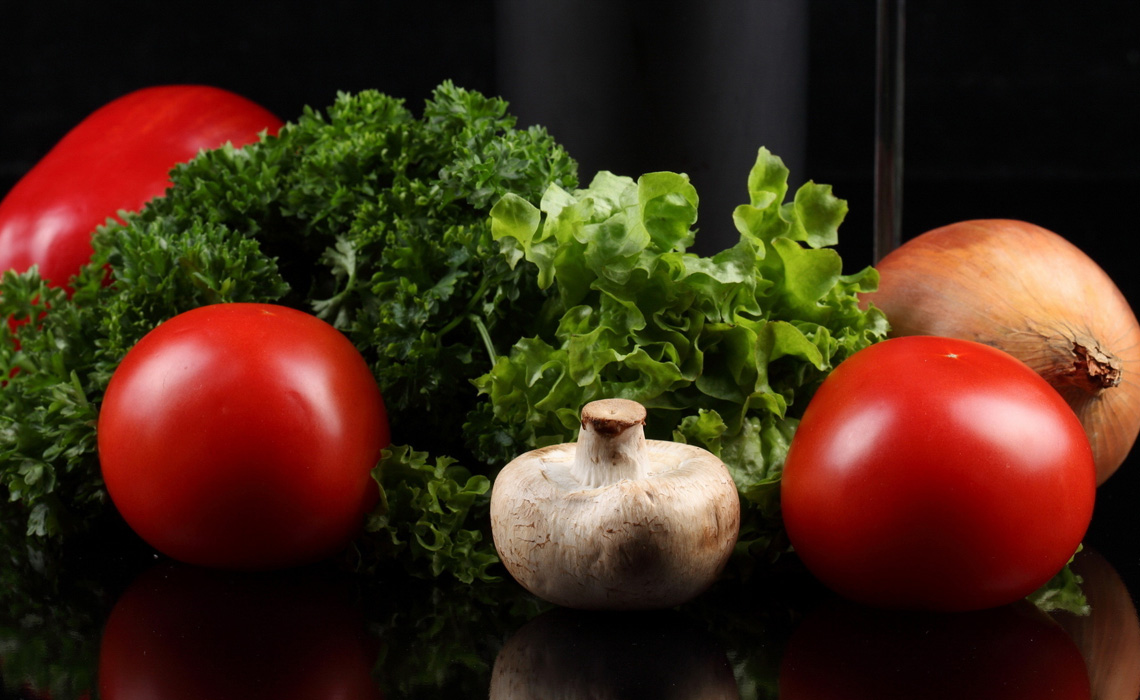 Fresh tomatoes, lettuce, parsley, and a mushroom on a black surface.