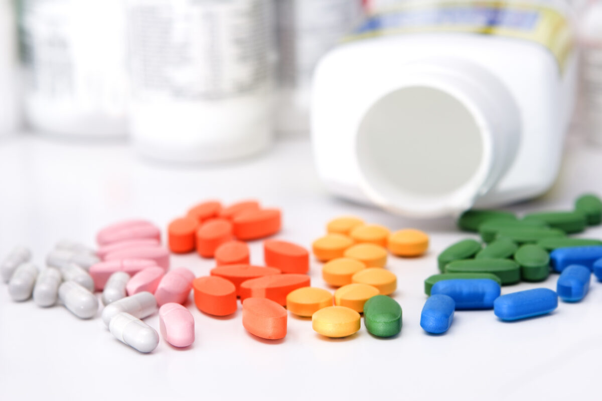 Various colorful pills spilled from a white bottle on a surface.