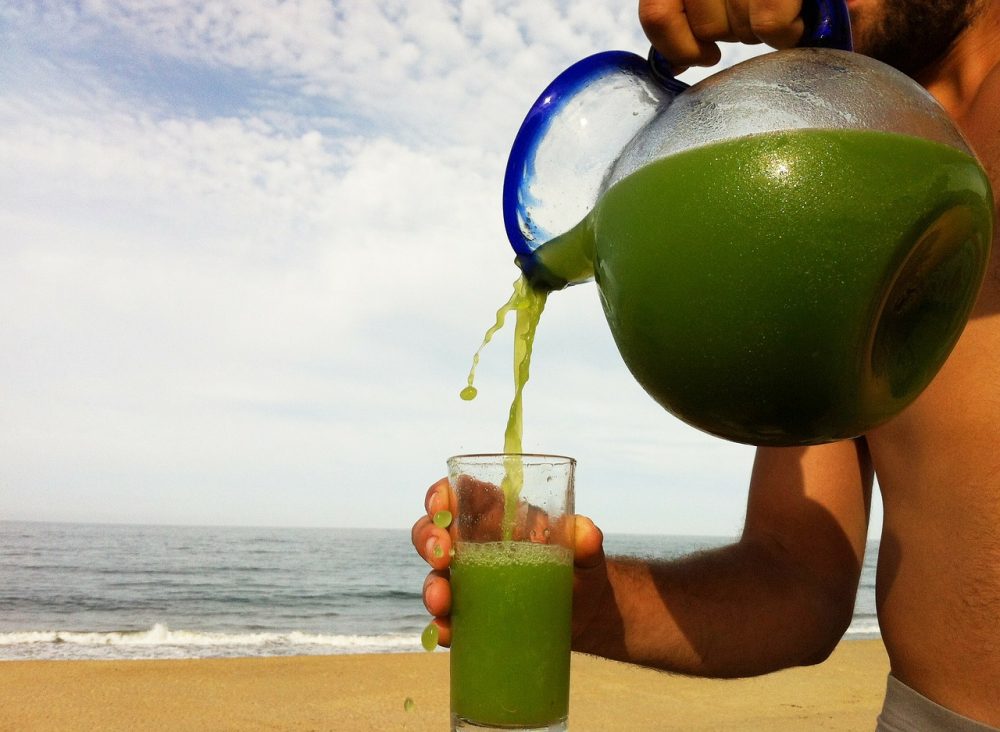 Pouring fresh green juice into a glass at the beach.