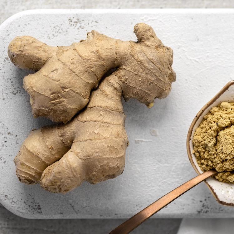 Fresh ginger root with a bowl of ground ginger powder and a spoon.