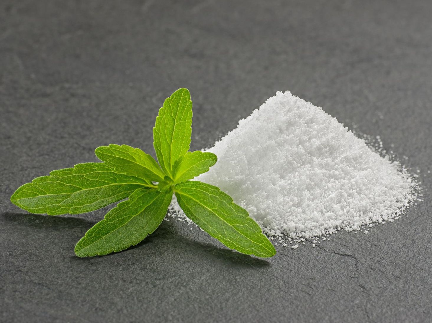 Fresh green stevia leaves beside a pile of white stevia powder.